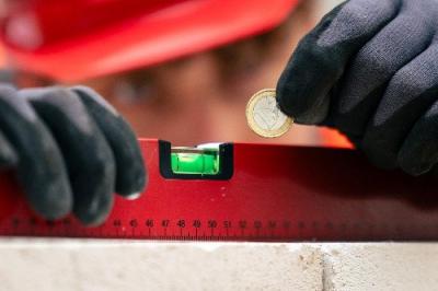 Eine Hand in Arbeitshandschuhen hält eine Münze neben eine Wasserwaage. Eine Hand in Arbeitshandschuhen hält eine Münze neben eine Wasserwaage.