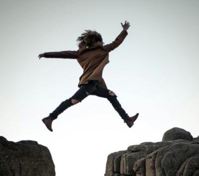 Eine Frau springt über einen Abgrund zwischen zwei Bergen und überwindet die Lücke. Eine Frau springt über einen Abgrund zwischen zwei Bergen und überwindet die Lücke.