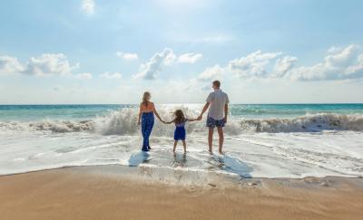 Frau, Kind und Mann Hand in Hand am Strand, aufs Meer blickend