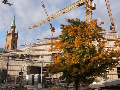 Baustelle. Im Vordergrund steht ein Laubbaum mit bunten Blättern.