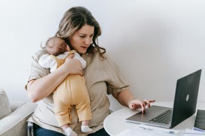 Eine Frau mit Baby auf dem Arm arbeitet am Laptop