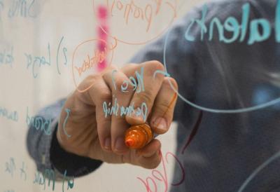 Die Hand eines Menschen, der auf ein Whiteboard schreibt