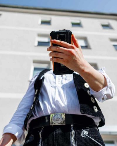 Person in Arbeitskleidung, das Gesicht von einem Handy verdeckt.