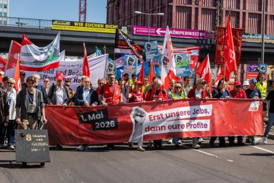 Demonstrationszug mit Transparent "Erst unsere Jobs, dann eure Profite"